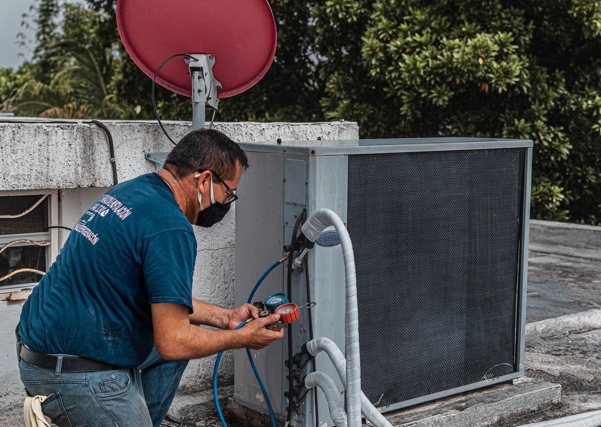 Technician servicing an outdoor air conditioning unit with gauges